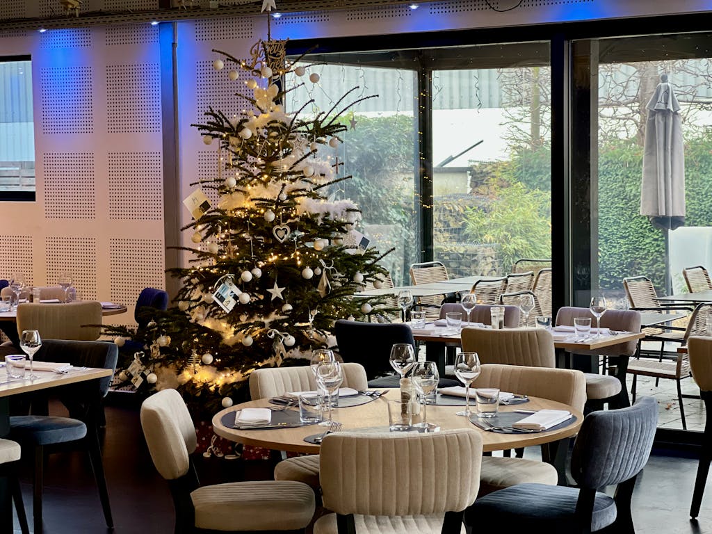 Elegant restaurant interior with decorated Christmas tree and set tables for a holiday ambiance.